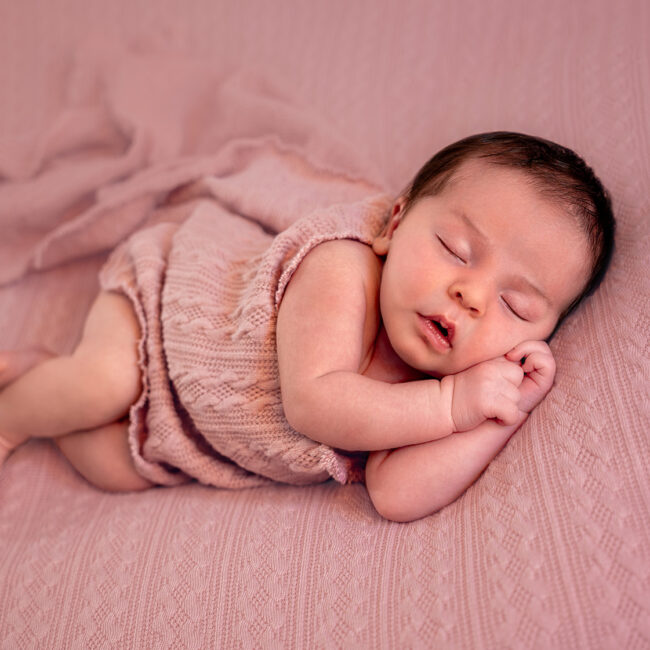 Newborn baby girl sleeping in soft beige blanket with floral headband – professional newborn photography by Joanna